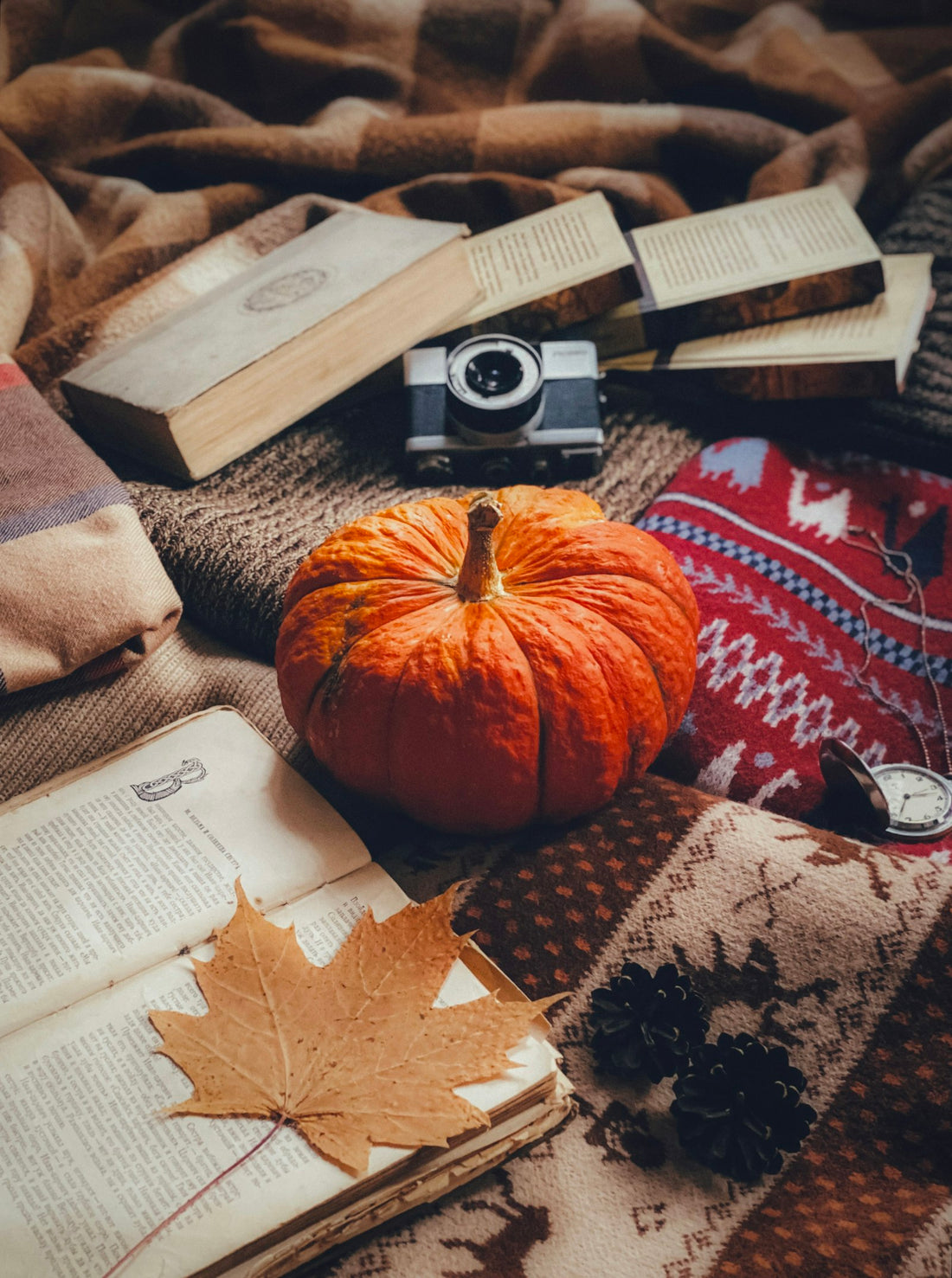 A cozy stack of books with a small pumpkin on a blanket, set up for a fall reading aesthetic